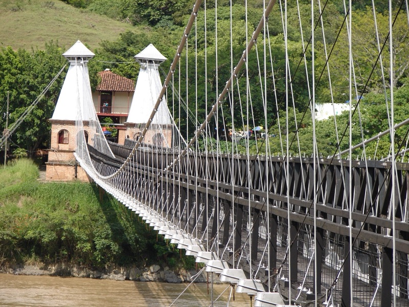 The Puente de Occidente, a long wooden suspension bridge with white towers, crossing the Cauca River near Santa Fe de Antioquia