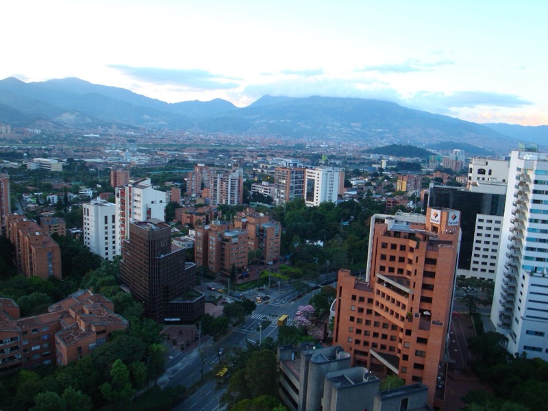Brick high-rises and green trees in El Poblado, with the mountains of the Aburrá Valley behind