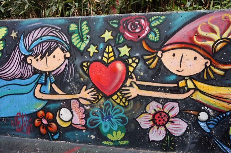 A colorful mural of two children holding a red heart among flowers and birds in Comuna 13