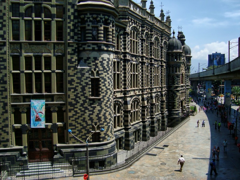 The black and gray checkerboard stone facade and domed towers of the Palacio de la Cultura in Medellín, beside the elevated metro line
