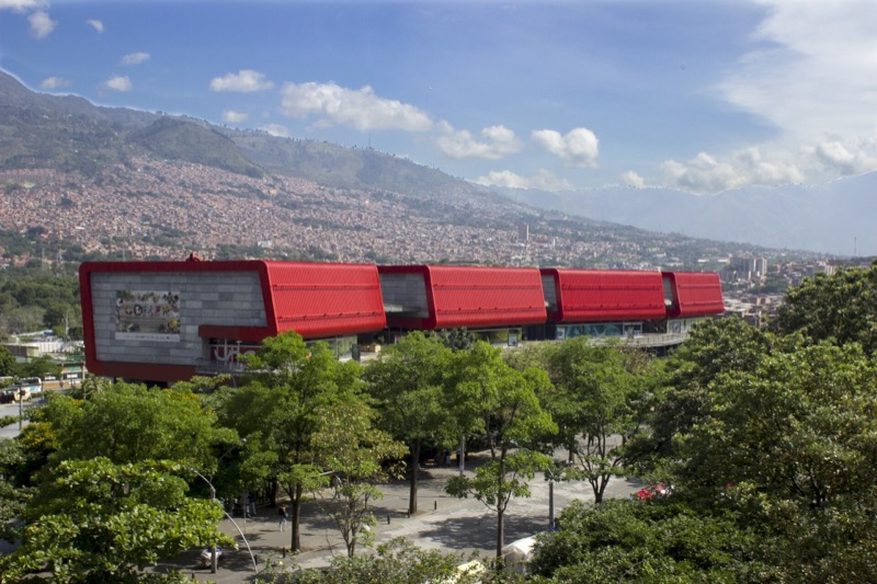 The four red boxes of Parque Explora's building, with Medellín's hillside neighborhoods and mountains behind